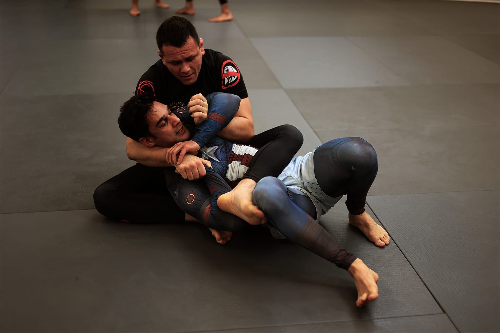 Two no-gi grapplers rolling on the mats, one working for control from the back